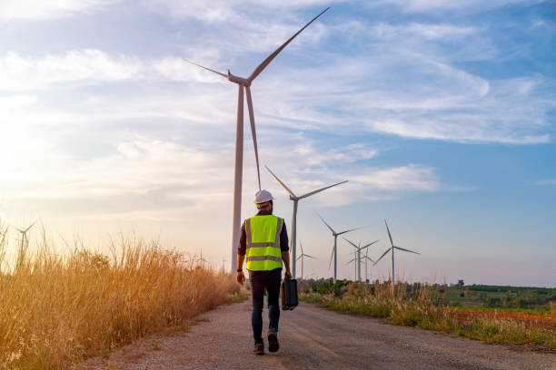 istock Engineer wearing uniform ,helmet hold document inspection work in wind turbine farms rotation to generate electricity energy. Green ecological power energy generation wind sustainable energy concept. 1388878913