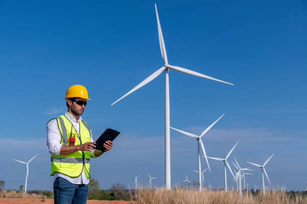 istock Engineer wearing uniform ,helmet hold document inspection work in wind turbine farms rotation to generate electricity energy. Green ecological power energy generation wind sustainable energy concept. 1388879097