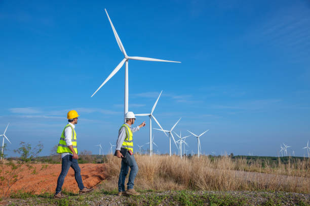 istock Engineer wearing uniform ,helmet hold document inspection work in wind turbine farms rotation to generate electricity energy. Green ecological power energy generation wind sustainable energy concept. 1388879666