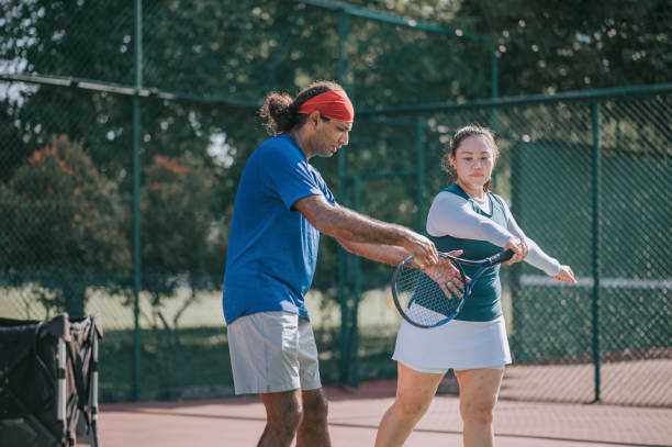 Asian Chinese mid adult woman learning tennis from her coach in tennis court during weekend morning Asian Chinese mid adult woman learning tennis from her coach in tennis court during weekend morning tennis coach stock pictures, royalty-free photos & images