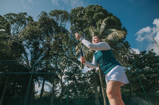 Asian Chinese woman practicing serving in tennis court during weekend morning
