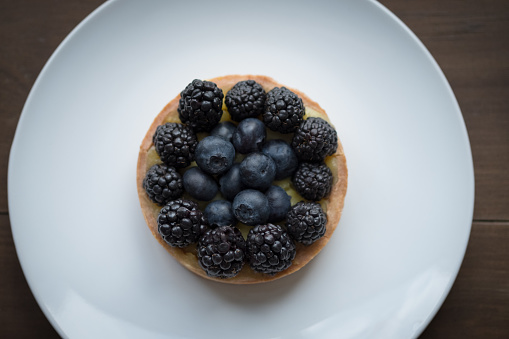 French pastry - fresh blackberry and blueberry tart on white plate served in Montreal, Quebec, Canada.