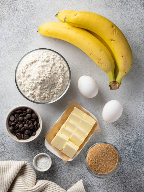istock Banana bread (cake, pancakes or muffins) ingredients top view. Flour bowl, white eggs, butter, brown sugar, chocolate chips, bananas.Close-up food. 1388891740