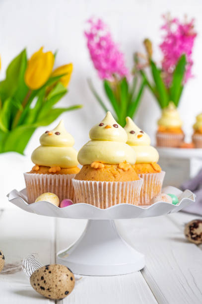 istock Cute Easter chick cupcakes. Vanilla cupcakes with buttercream on a white stand with fresh flowers on a white wooden background. Copy space. 1388893758