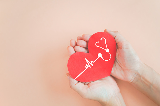 hand holding red heart with heartbeat and stethoscope icon on grunge orange pastel background for health check up concept including copy space