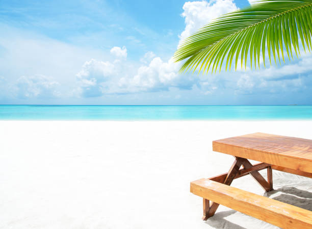 Wooden table under palm leaves at tropical white beach