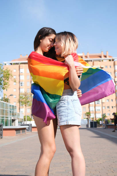 istock Young lesbian couple smiling and hugging wrapped in a rainbow flag. 1388895823