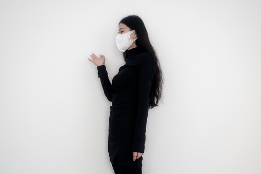 A woman in a mask standing on a white wall