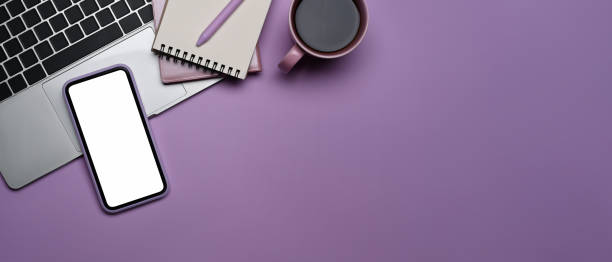istock Mobile phone with empty screen, laptop computer, coffee cup and notebook on purple background. Top view. 1388897030
