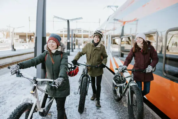 Friends waiting and boarding a train with their fatbikes. They're going for a bike ride in nature on a sunny day.