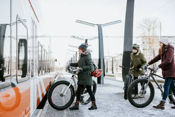 Friends waiting and boarding a train with their fatbikes. They're going for a bike ride in nature on a sunny day.