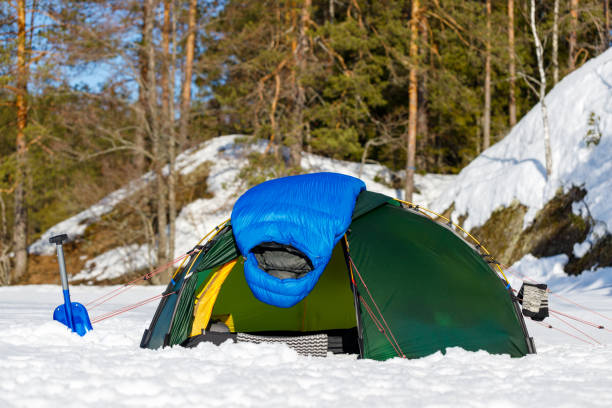 blauer daunenschlafsack zum trocknen auf einem grünen zelt im winterwald. - snow dune stock-fotos und bilder