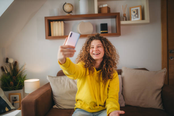 istock Young woman with curly hair in a video from a conference using a mobile phone while relaxing on the sofa 1388901323