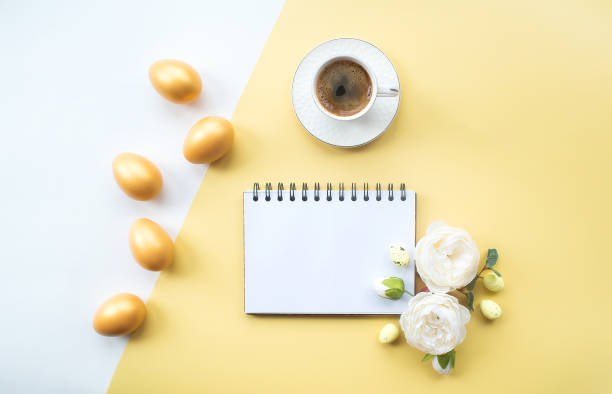 istock Golden easter eggs, coffee mug, delicate flowers and notebook with place for text on on yellow background. Trendy flat lay. minimal concept. 1388901874