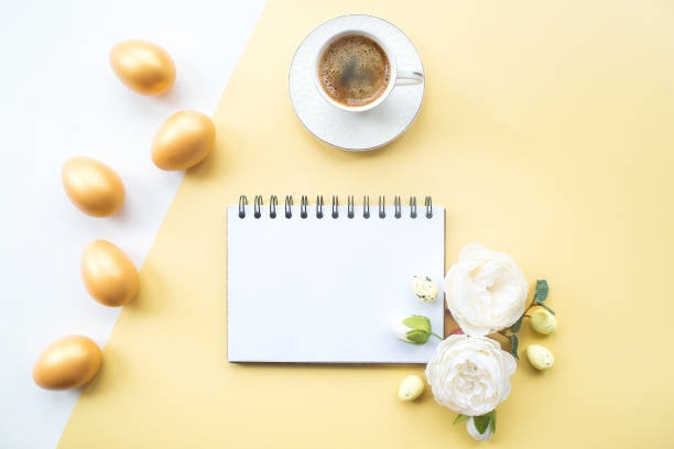 istock Golden easter eggs, coffee mug, delicate flowers and notebook with place for text on on yellow background. Trendy flat lay. minimal concept. 1388901880