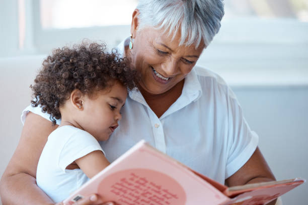 aufnahme einer reifen großmutter, die ihrer enkelin zu hause eine geschichte vorliest - grandparent family reading inside of stock-fotos und bilder