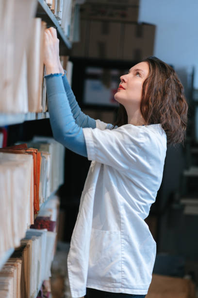 istock University post-grad student in lab coat looking for files on shelf in the library 1388905246
