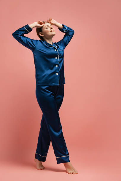 retrato de una joven en pijama de seda azul posando aislada sobre el fondo rosa del estudio - ropa de dormir fotografías e imágenes de stock