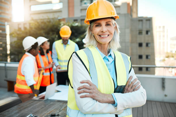 istock Shot of a mature contractor standing outside with her arms folded while her colleagues work behind her 1388907342