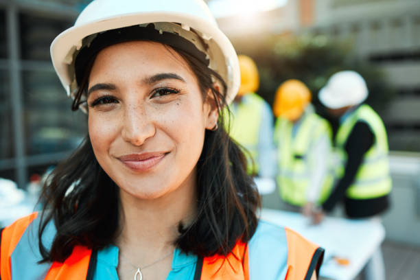 istock Shot of an attractive young contractor standing outside while her colleagues work behind her 1388907353