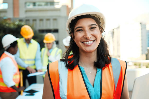 istock Shot of an attractive young contractor standing outside while her colleagues work behind her 1388907361