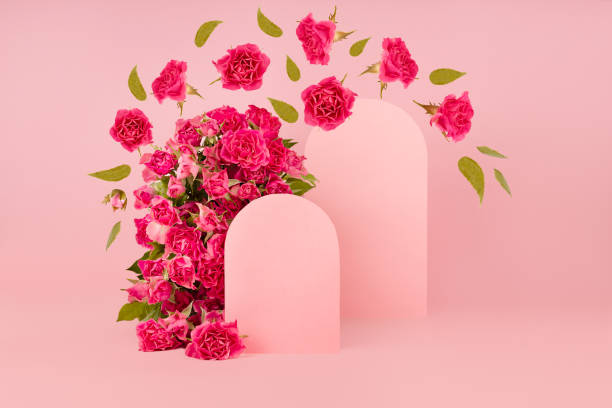 istock Spring fresh pink roses as arch with two empty rounded doors as podiums mockup with fly green leaves, buds as swirl for presentation cosmetic products, goods, advertising, design on pink background. 1388907442