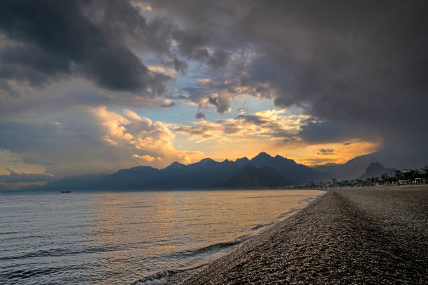 The center of attraction is the world-famous Konyaaltı beach. The view of the Mediterranean Sea and Taurus Mountains, mountain ranges in winter. Closed air, sunset.The sun sets behind the mountains, the sea without waves.