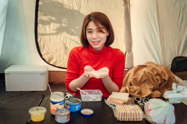 A woman traveler is preparing sandwiches for her dinner inside the tent. stock photo