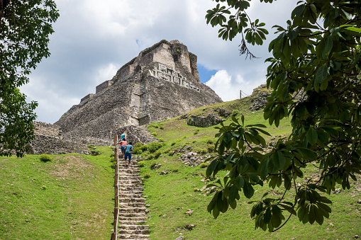 San Ignacio, Belize - 24 August 2019: Tourists climbing the steep stairs to the sunlit Maya ruin 'El Castillo' at the archeological site Xunantunich