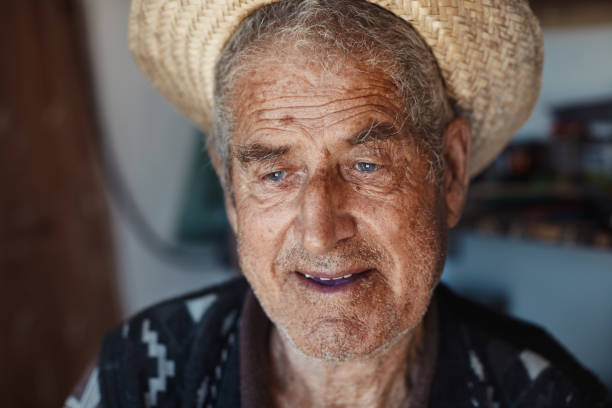 Portrait of elderly Asian man farmer wears a hat, blue shirt standing and looking at camera, isolated on white background.
