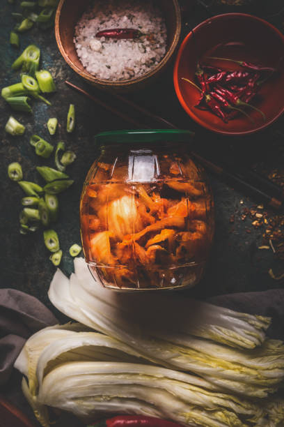 Fermented chinese cabbage marinated in hot chili sauce, kimchi,  in glas jar on rustic background with ingredients. stock photo