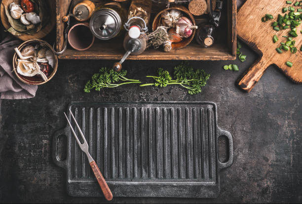 Grill or BBQ food background with empty cast iron grill griddle and meat fork  on roast rustic kitchen table.