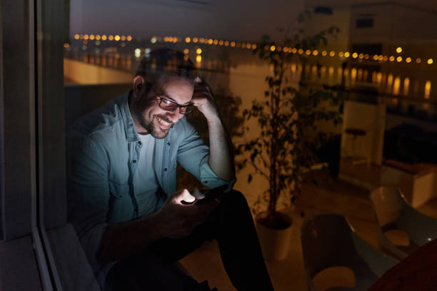 istock Happy man using cell phone by the window at night. 1388911567