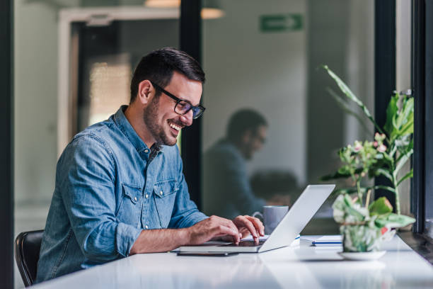 Smiling adult businessman, making an advertisement for his company. Delighted adult man, working on a company slogan, on his laptop. teamwork slogan stock pictures, royalty-free photos & images