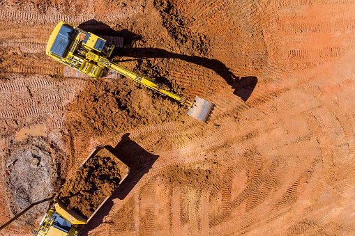 Aerial top down view of an excavator loading earth into a dump truck in a under construction site