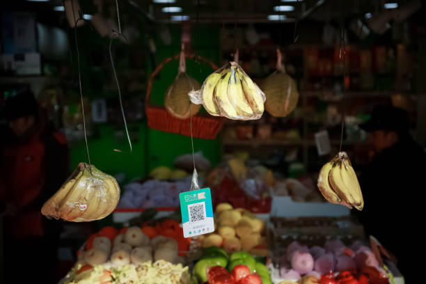 2021, June 5th, China, Shanghai. A typical street vendor, this one sells fruits. We see bananas hanging from the ceiling and a QR code for payment. In the background are a variety of fruits laid out on a table.