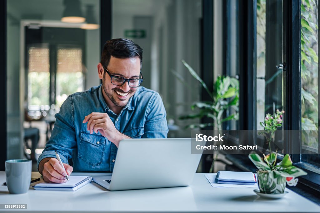 Lovely business man, attending a meeting online, writing stuff down. Cheerful adult man with glasses, taking notes on the conference call. Men Stock Photo
