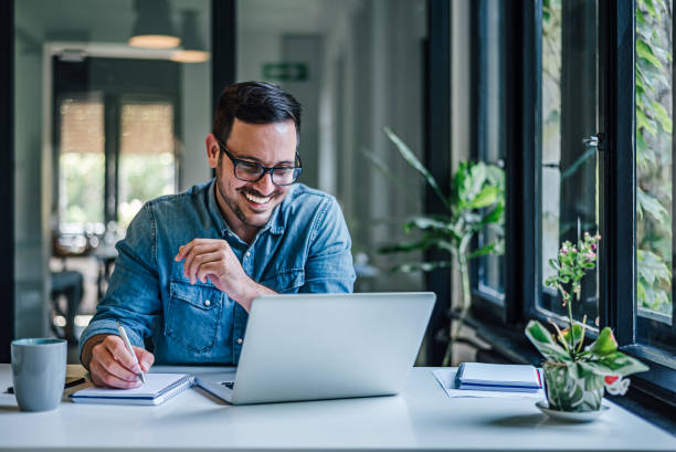 Lovely business man, attending a meeting online, writing stuff down. Cheerful adult man with glasses, taking notes on the conference call. effortless stock pictures, royalty-free photos & images