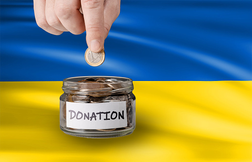 Donation for Ukraine concept. donation jar with Ukrainian flag. Hand putting Coins in glass jar with donation. hand putting penny in money jar on ukranian flag background