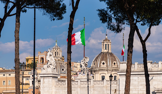 A picture of two Italian flags next to some landmarks as seen through trees.