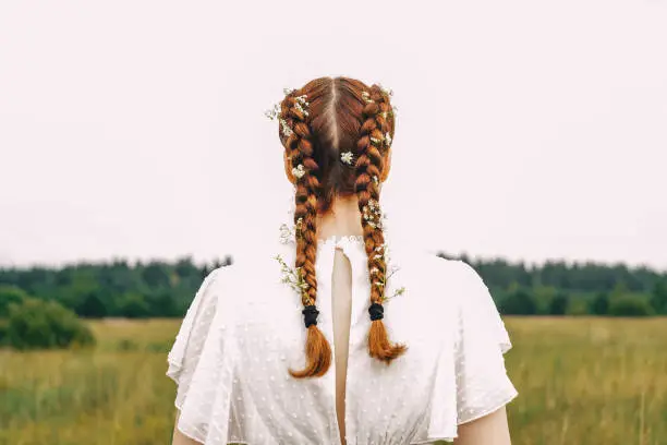 Head of a woman in a field, rear view. Flowers in pigtails. White dress and white sky, copy space.