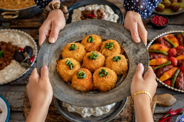 rodzinny obiad z wieloma potrawami na stole i deserem z rąk dwóch kobiet. lokalne desery o nazwie kadayıf lub kadayif . - traditional foods zdjęcia i obrazy z banku zdjęć