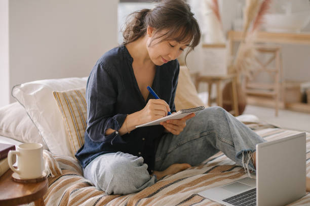 istock Young asian woman looking at laptop screen and making some notes while working at home 1388915923