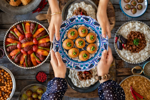 Family dinner with many foods on the table and dessert at the hands of two woman. Local desserts named şekerpare and kemalpaşa tatlısı. Dining table with top view. lebanese culture stock pictures, royalty-free photos & images