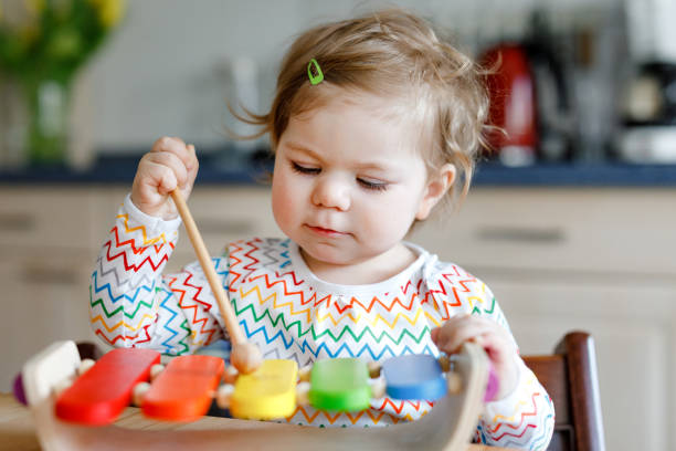 Adorable cute beautiful little baby girl playing with educational wooden music toy at home. Happy excited toddler child learn to play colorful rainbow xylophon. Early education, activity for children. stock photo