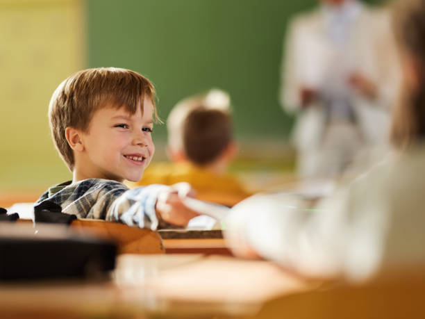 istock Happy schoolboy giving a note to his classmate in the classroom. 1388919120