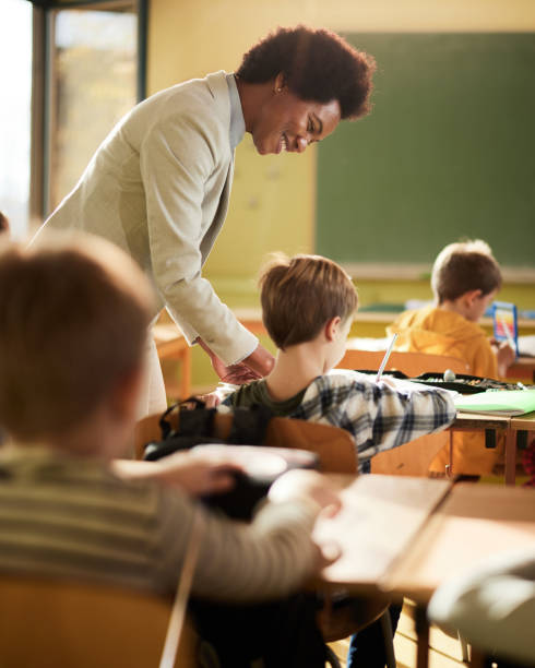 istock Happy black professor assisting schoolboy on a class at school. 1388919143