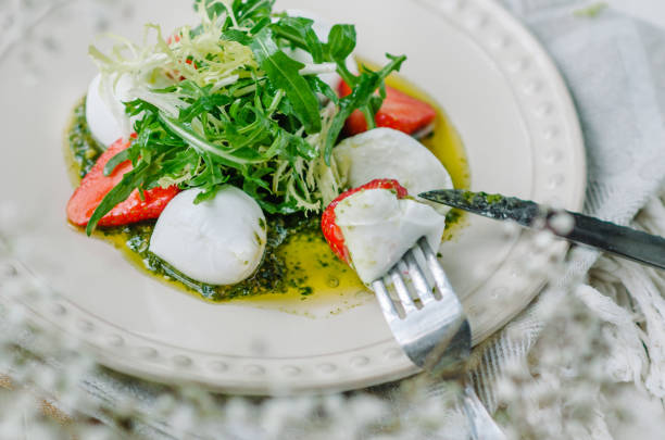 ensalada fresca ligera de verano. mozzarella de búfala con fresas, pesto, rúcula y lechuga. ensalada de degustación de primer plano con cuchillo y tenedor - caprese salad salad restaurant vinegar fotografías e imágenes de stock