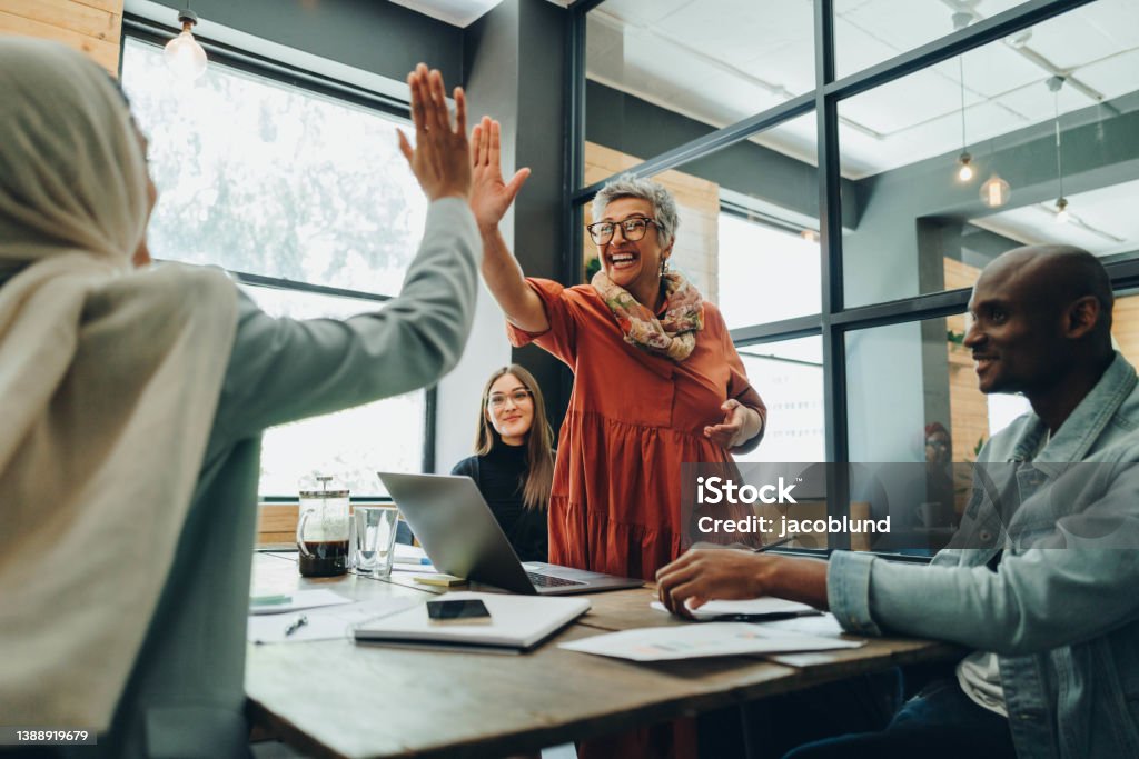 Two cheerful businesswomen celebrating their success Two successful businesswomen high fiving each other during an office meeting. Cheerful businesswomen celebrating their achievement. Happy businesspeople working as a team in a multicultural workplace. Business Stock Photo
