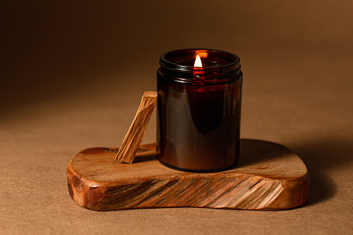 Burning candle in dark glasses on a wooden board.